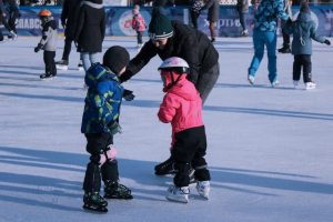 two children ice skating with the help of an adult